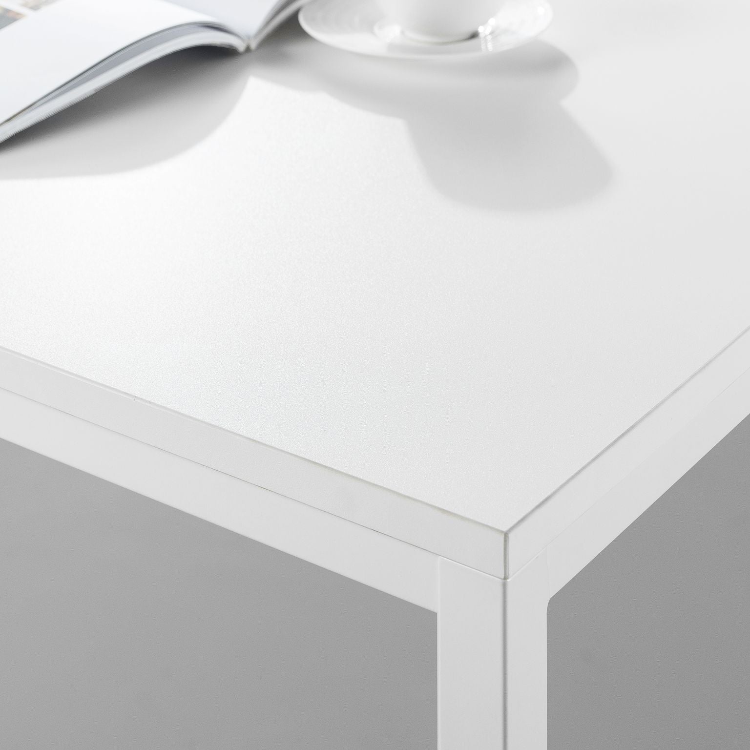 Modern white office desk with metal frame, open book and coffee cup on top