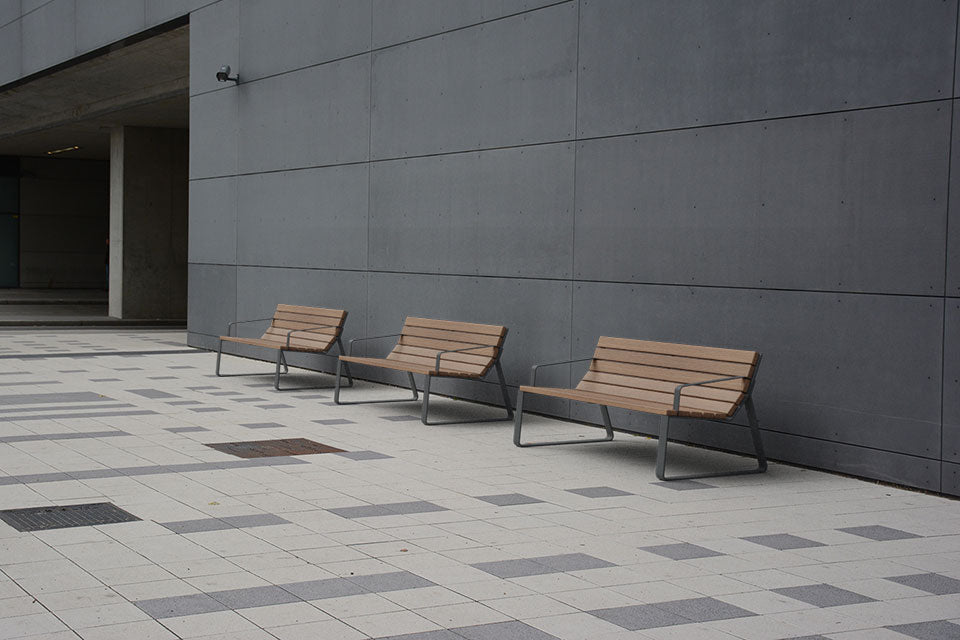 Three wooden benches against a gray concrete wall in an outdoor setting.