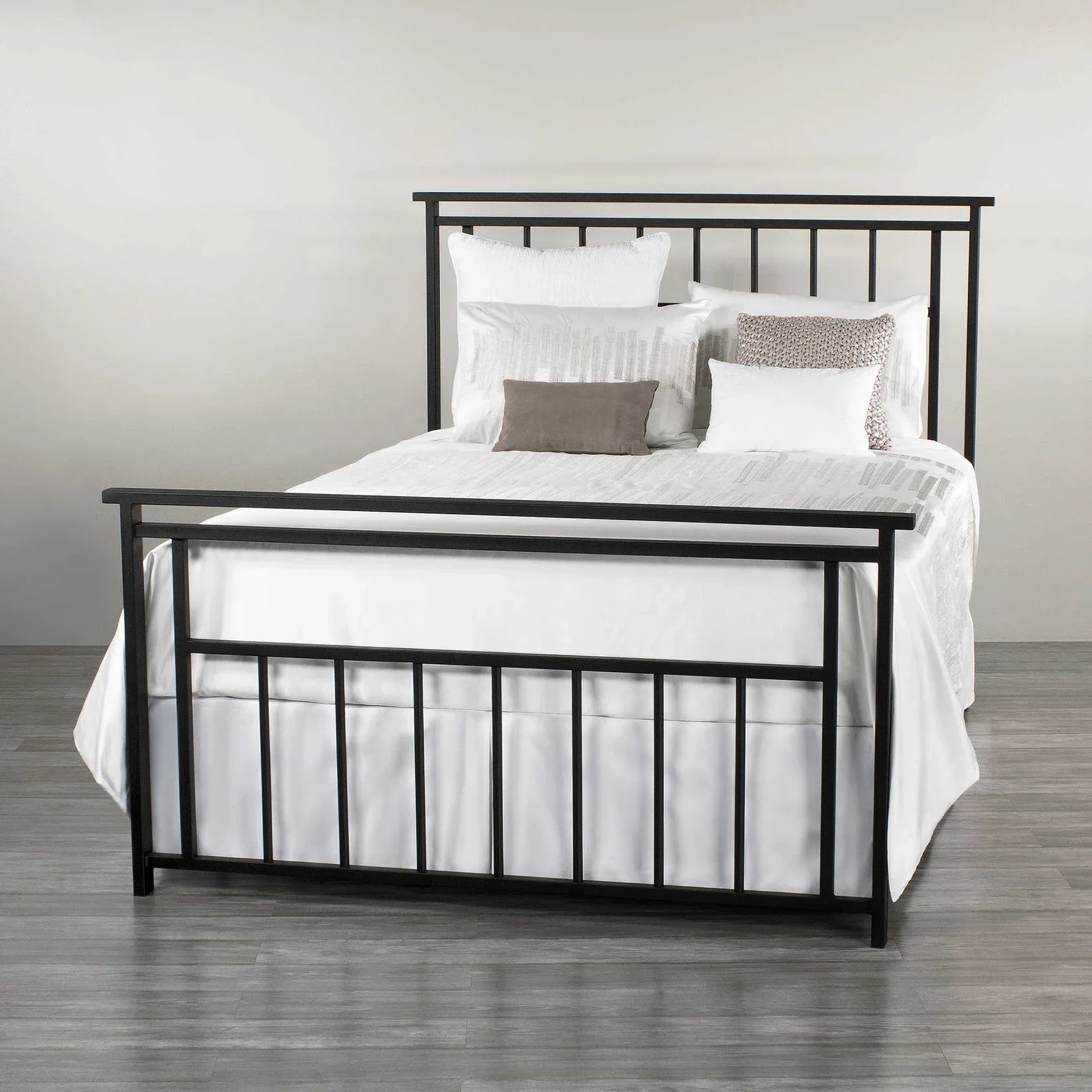 Modern black metal bed frame with white bedding and decorative pillows on grey floor