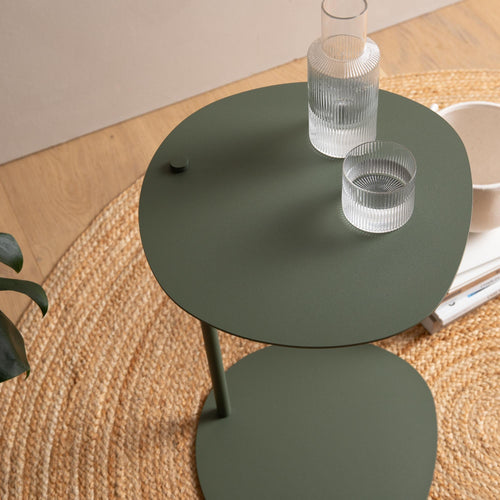 Modern green metal side table with glassware on a woven rug in a cozy room setting