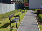 Modern outdoor park benches with black metal frames on grass beside a paved walkway