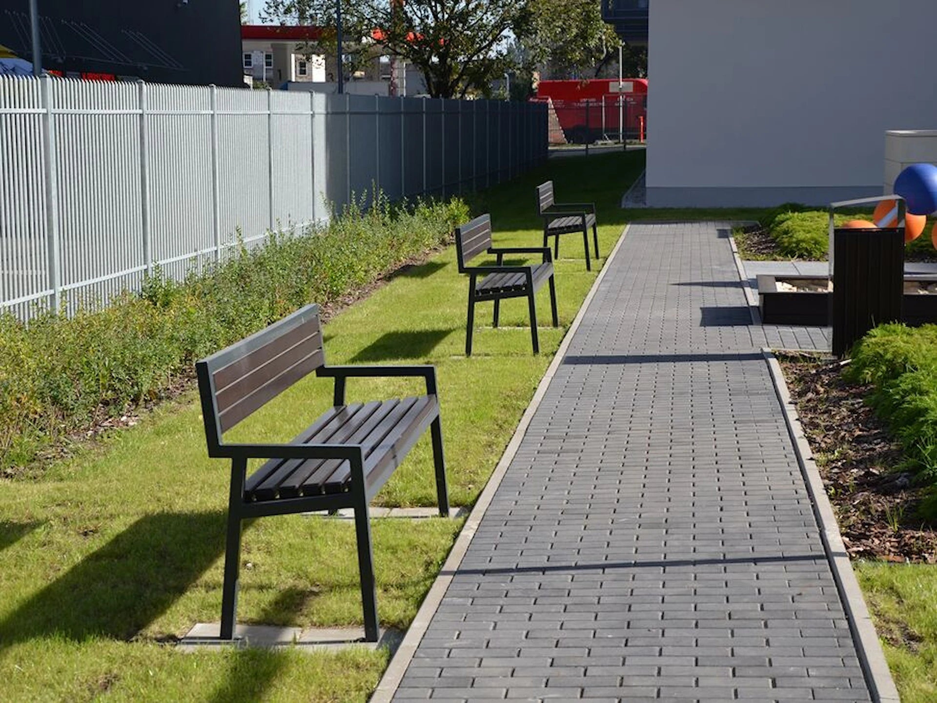 Modern outdoor park benches with black metal frames on grass beside a paved walkway