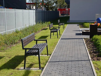 Modern outdoor park benches with black metal frames on grass beside a paved walkway