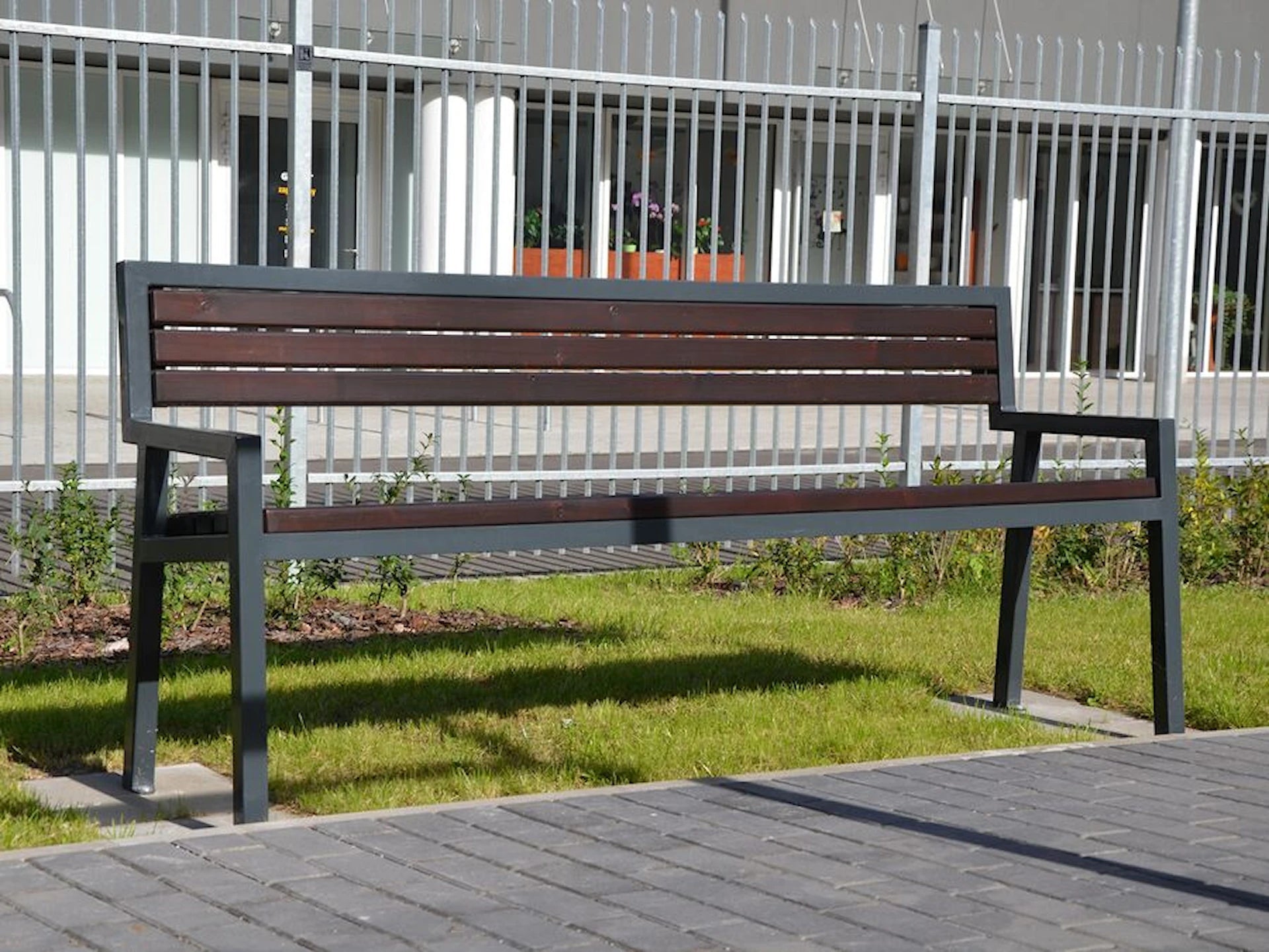 Outdoor modern park bench with metal frame and wooden slats on grass near sidewalk