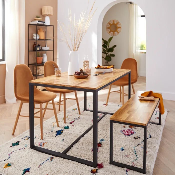 Solid oak bench with black metal frame in modern dining room, next to matching wood table and tan chairs