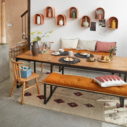 Solid oak bench with orange cushion in modern dining room, wood table and wall shelves.
