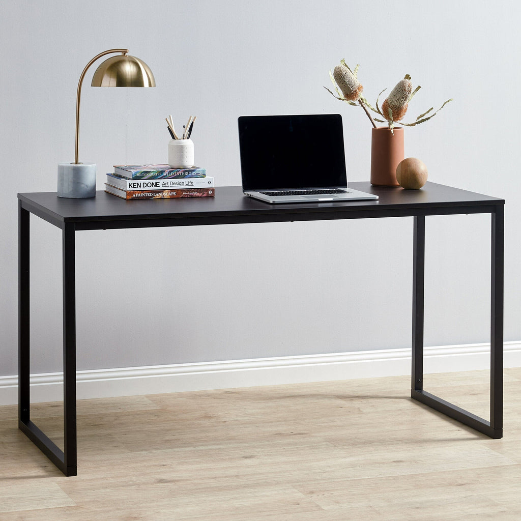 Modern black office desk with laptop, books, lamp, and decorative vase in a minimalist room