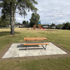 Outdoor wooden bench and table set on a paved area in a park with playground equipment