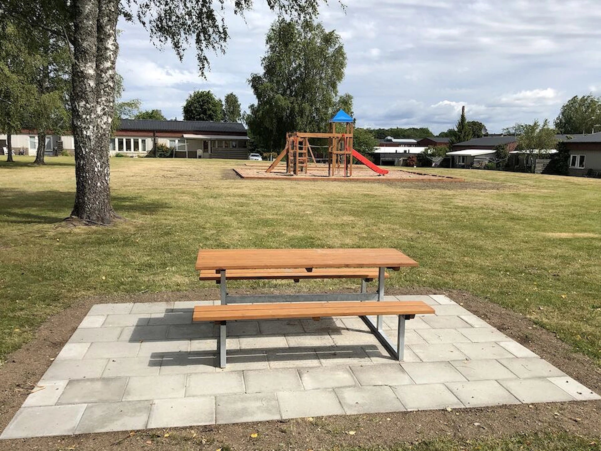 Outdoor wooden bench and table set on a paved area in a park with playground equipment