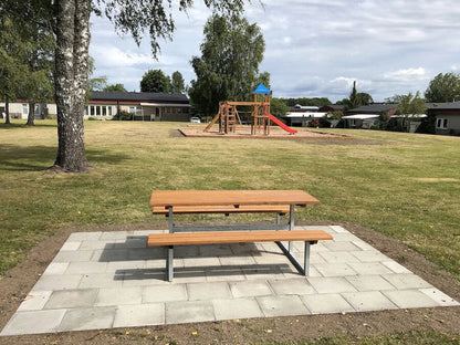 Outdoor wooden bench and table set on a paved area in a park with playground equipment