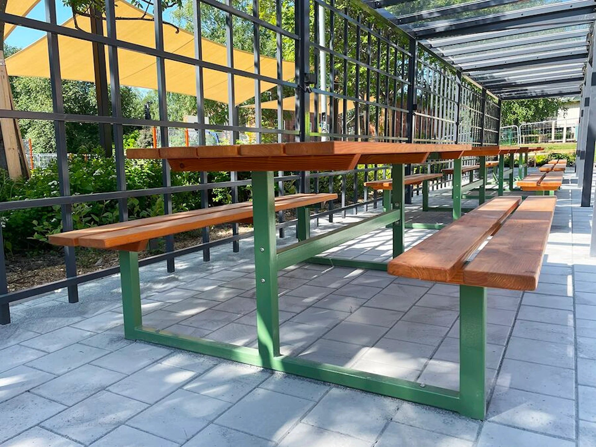 Outdoor wooden bench table set with green metal frame under covered patio, modern garden furniture