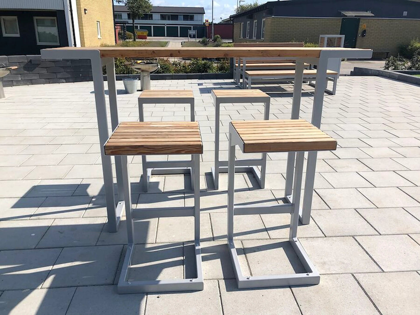 Modern outdoor bar set with metal frame and wooden stools on a paved patio