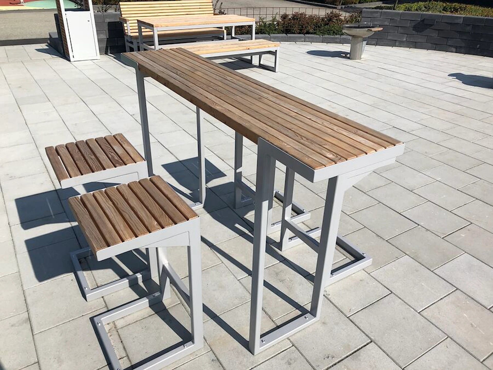 Outdoor modern bar table set with metal frame and wooden slat seats on paved patio