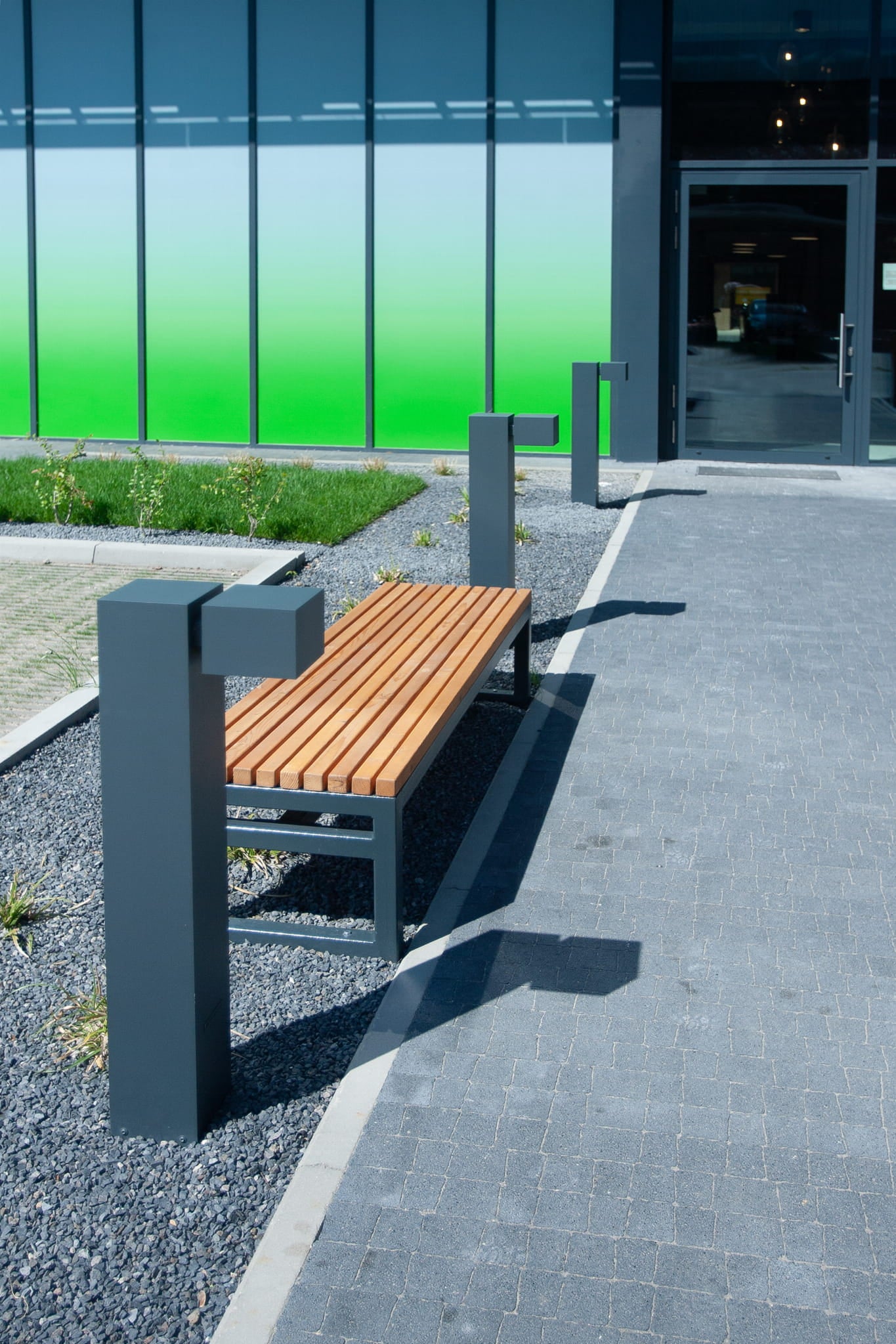 Modern outdoor 3-seater backless bench with wooden slats and metal frame on paved walkway