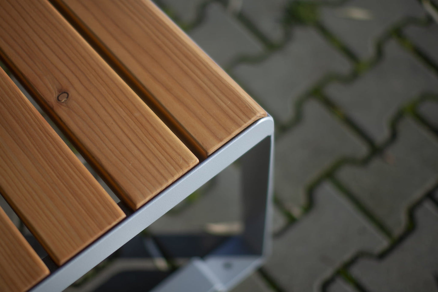 Modern outdoor backless bench with wooden slats and metal frame on stone paving