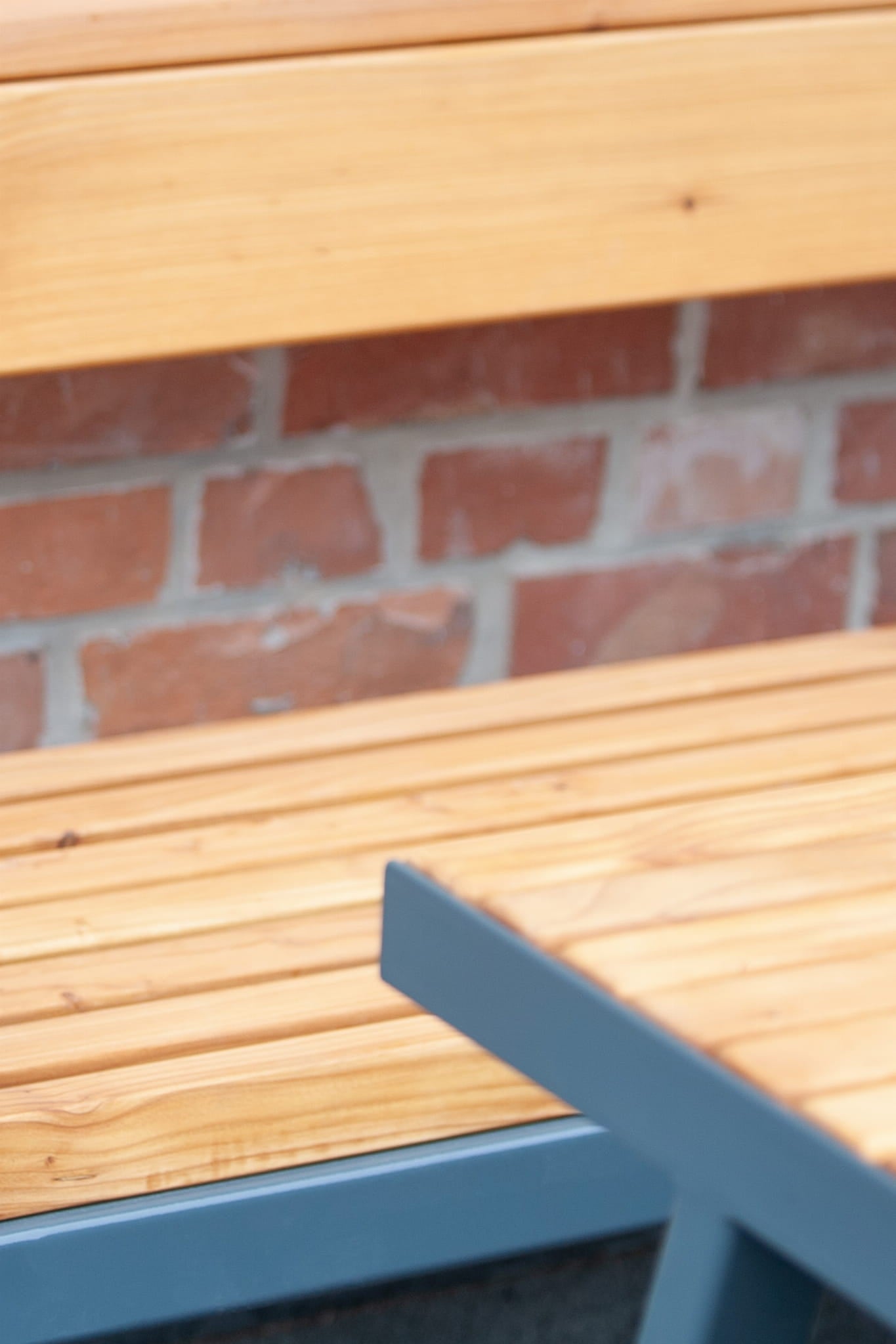 Modern public bench in wood and metal near a brick wall, close-up view