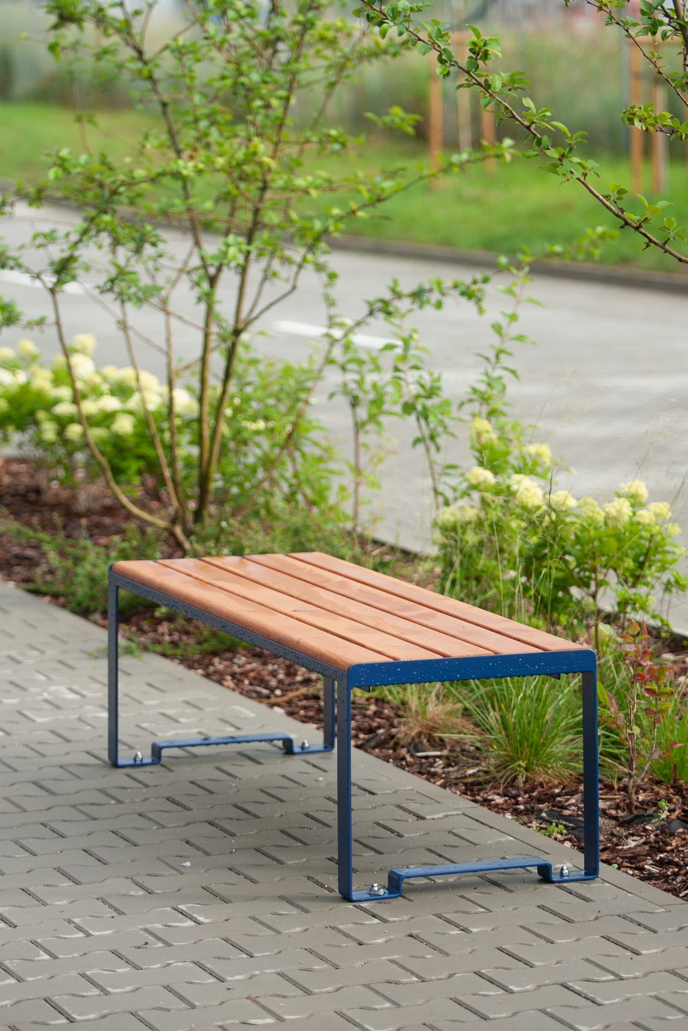 Modern backless three-seater wooden bench with metal frame placed outdoors on a sidewalk