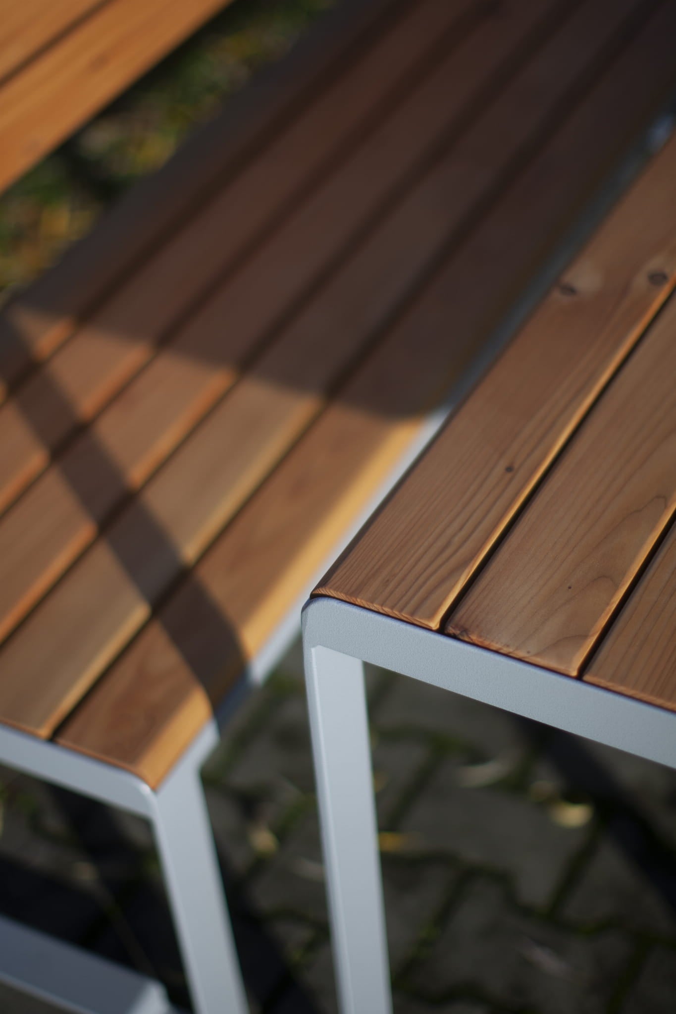 Close-up of slatted wood and metal 3-seater bench with backrest, outdoor setting