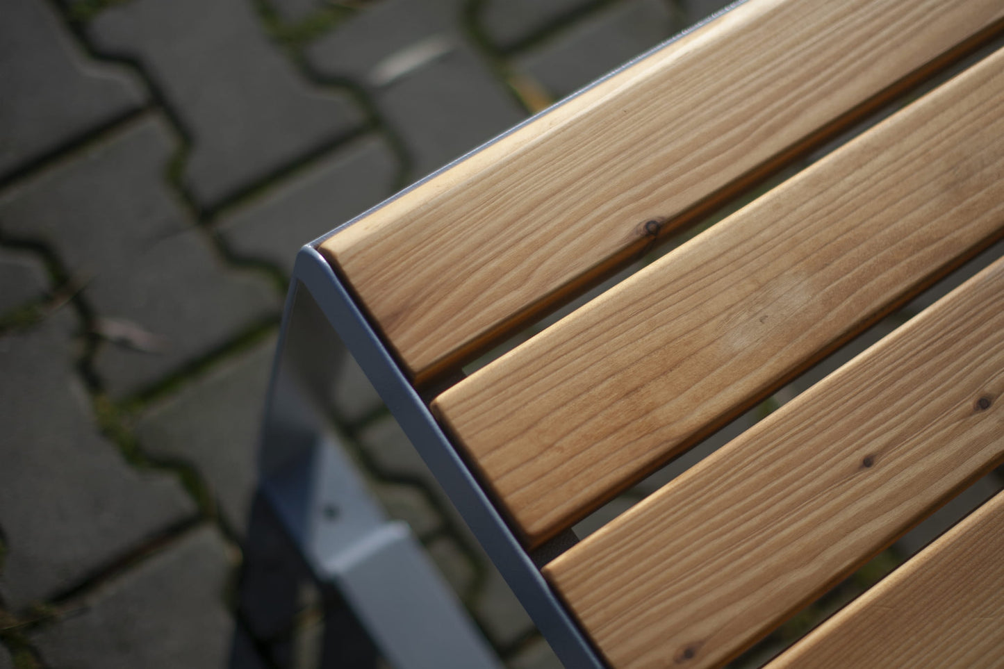 Close-up of modern outdoor wooden slat bench with metal frame on stone pavement