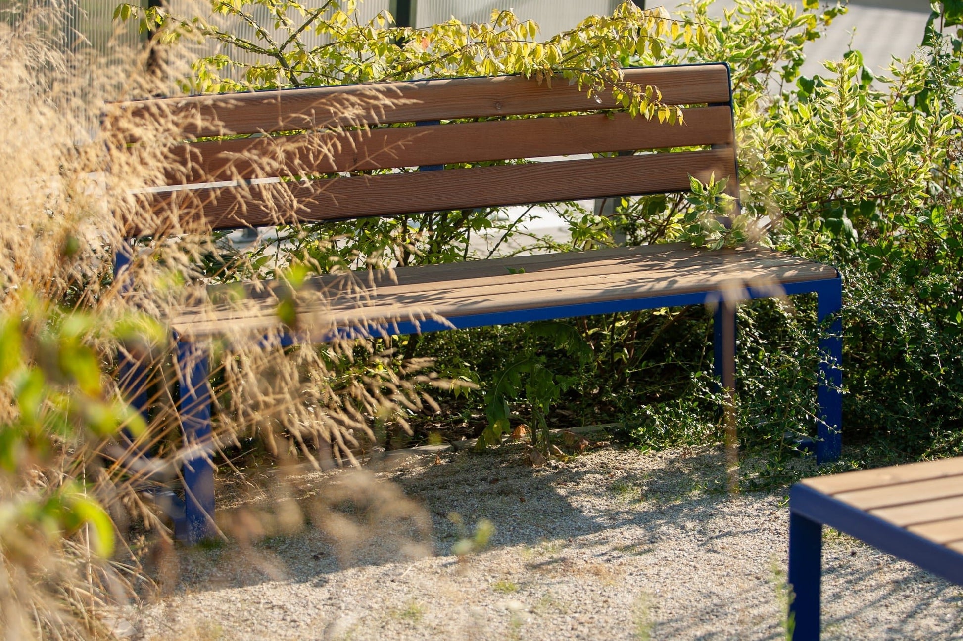 Outdoor wooden 3-seater bench with blue metal legs, placed in a garden setting