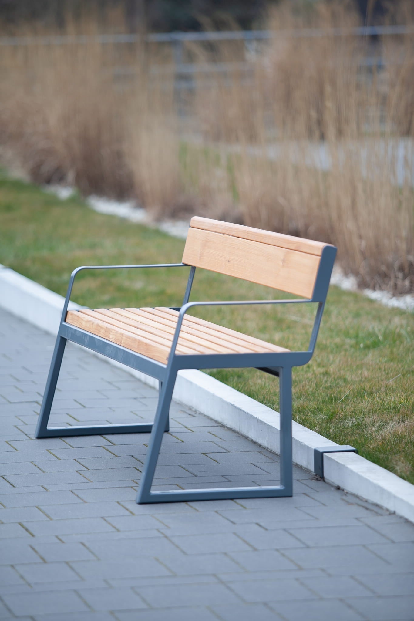 Modern 3-seater outdoor bench with backrest and armrests on a paved walkway