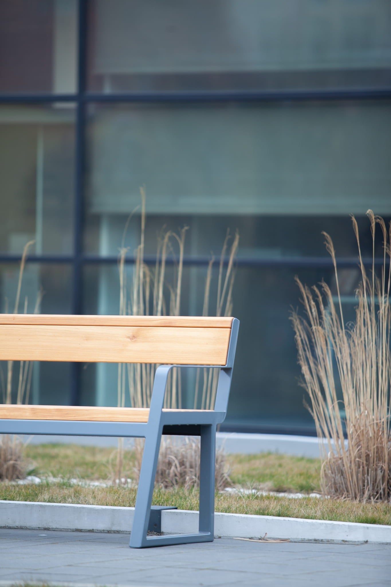 Modern 3-seater outdoor bench with wooden backrest and metal frame in landscaped area