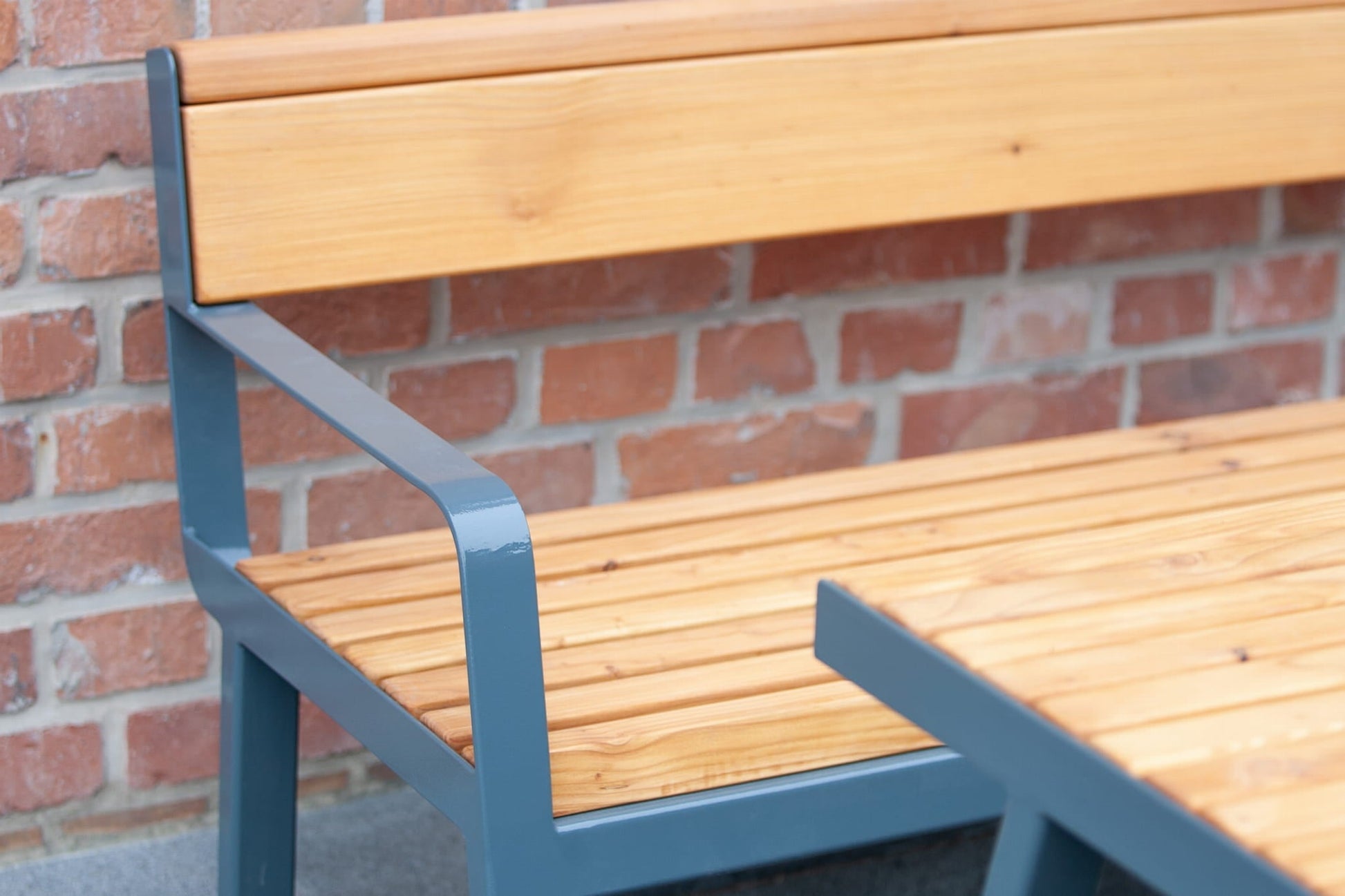 Outdoor 3-seater bench with wooden slats and metal armrest against a brick wall
