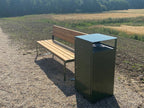 Modern green outdoor wastebasket next to wooden bench on gravel path in natural setting