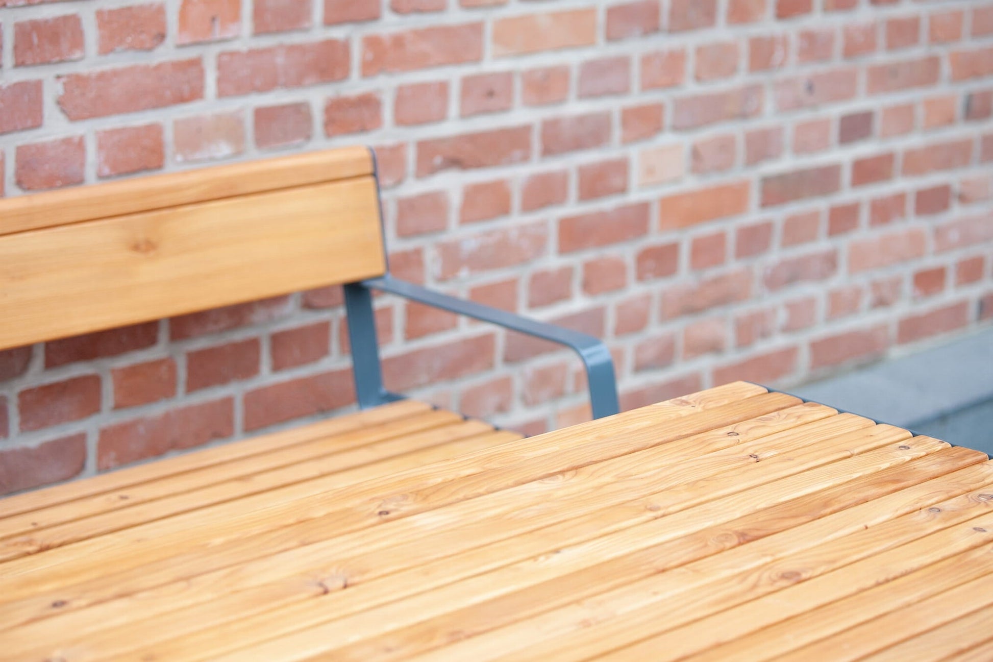 Sturdy outdoor wooden table and bench with metal armrest set against a brick wall