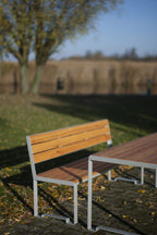 Modern outdoor wood and metal table with matching bench on a patio, park setting