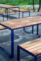Outdoor wooden table with blue metal frame and matching benches on patio