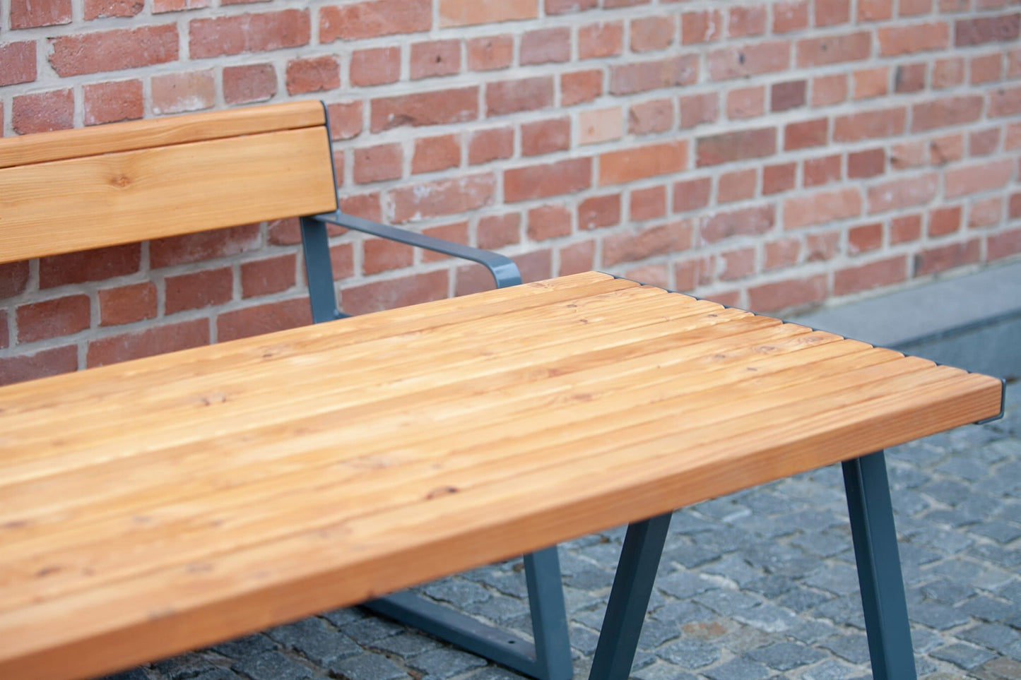 Sturdy outdoor wooden table with metal legs and bench on cobblestone patio by brick wall