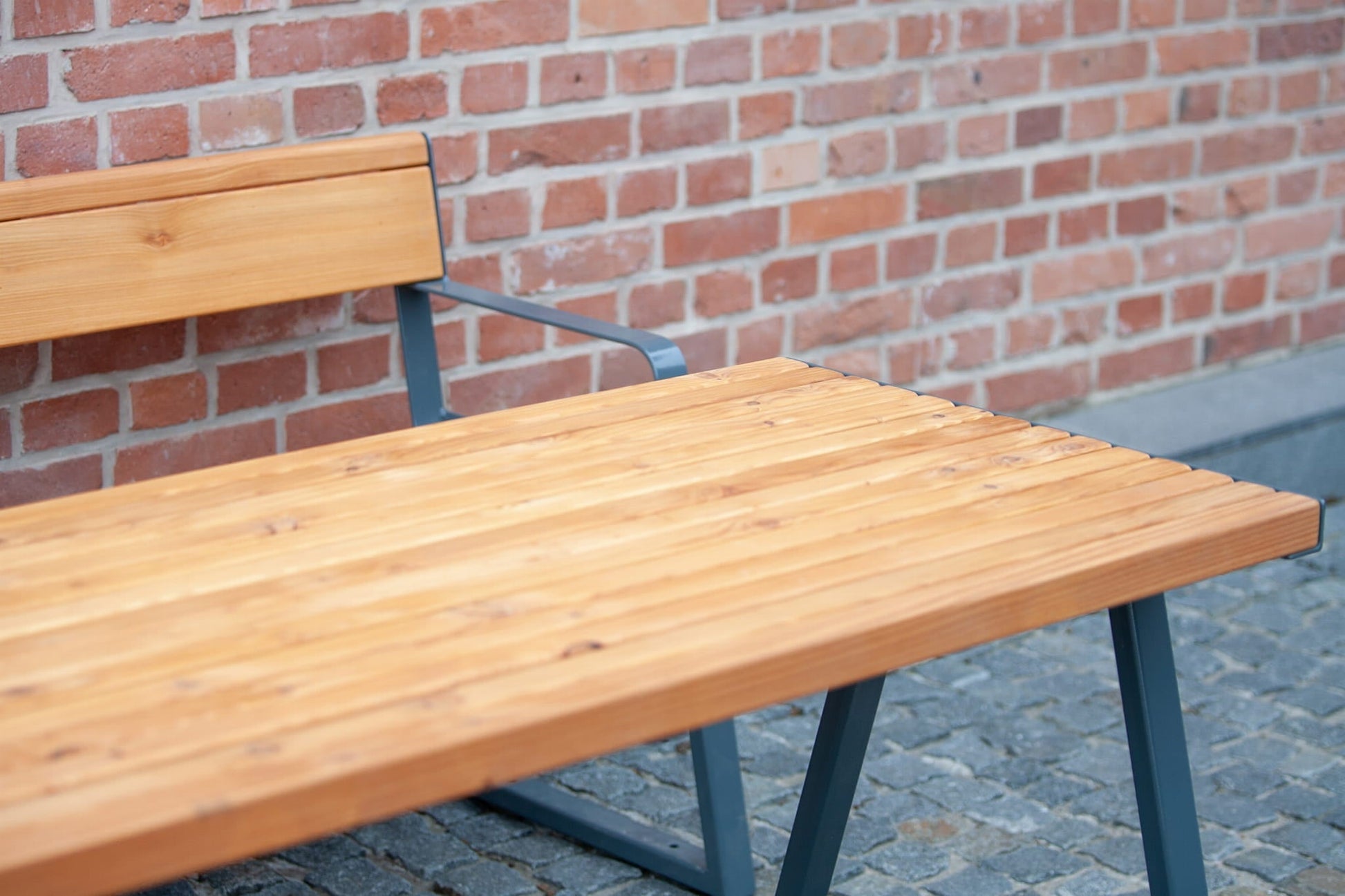 Sturdy outdoor wooden table with metal legs and bench on cobblestone patio by brick wall