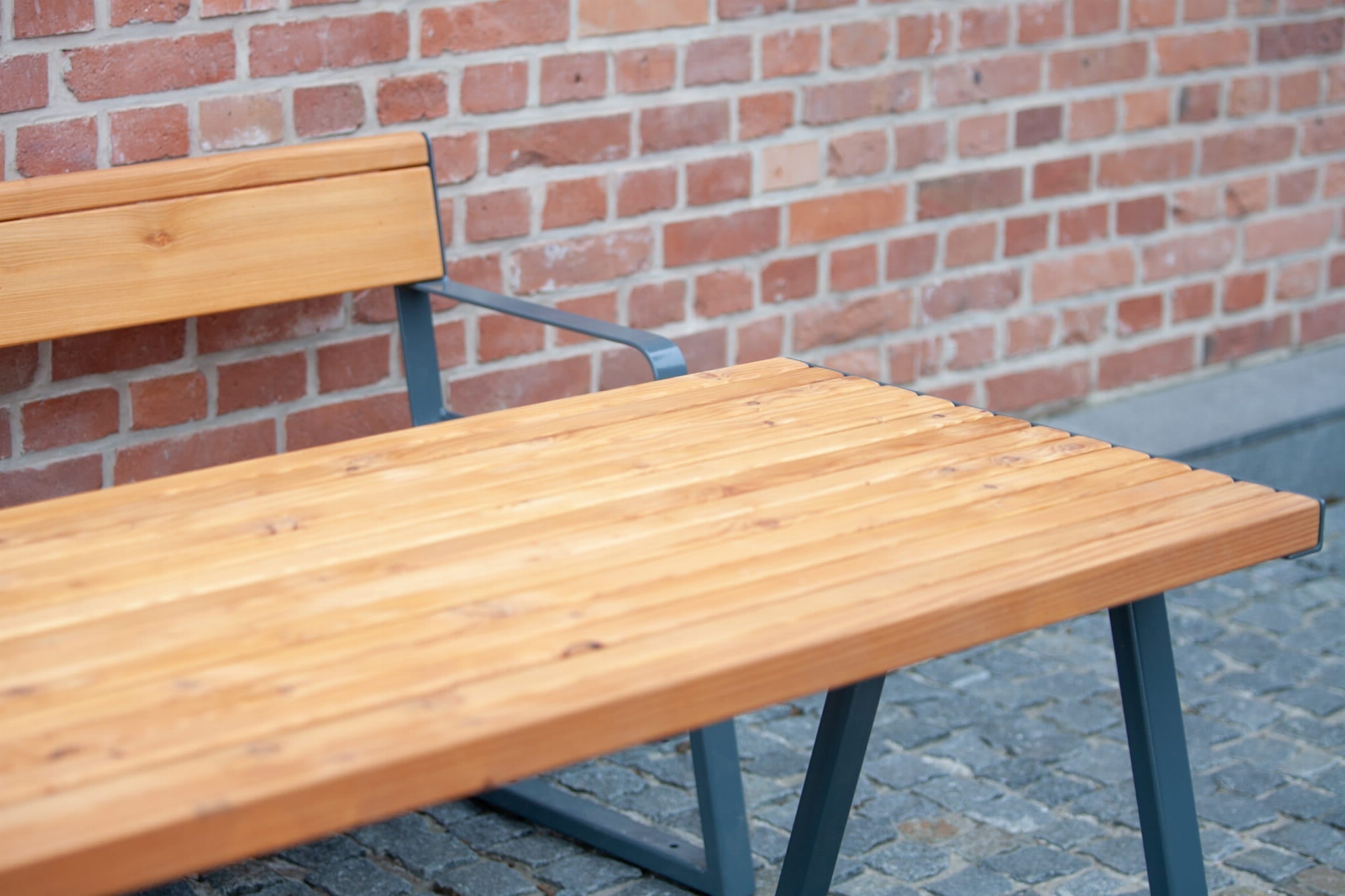 Sturdy outdoor wooden table with metal legs and bench on cobblestone patio by brick wall