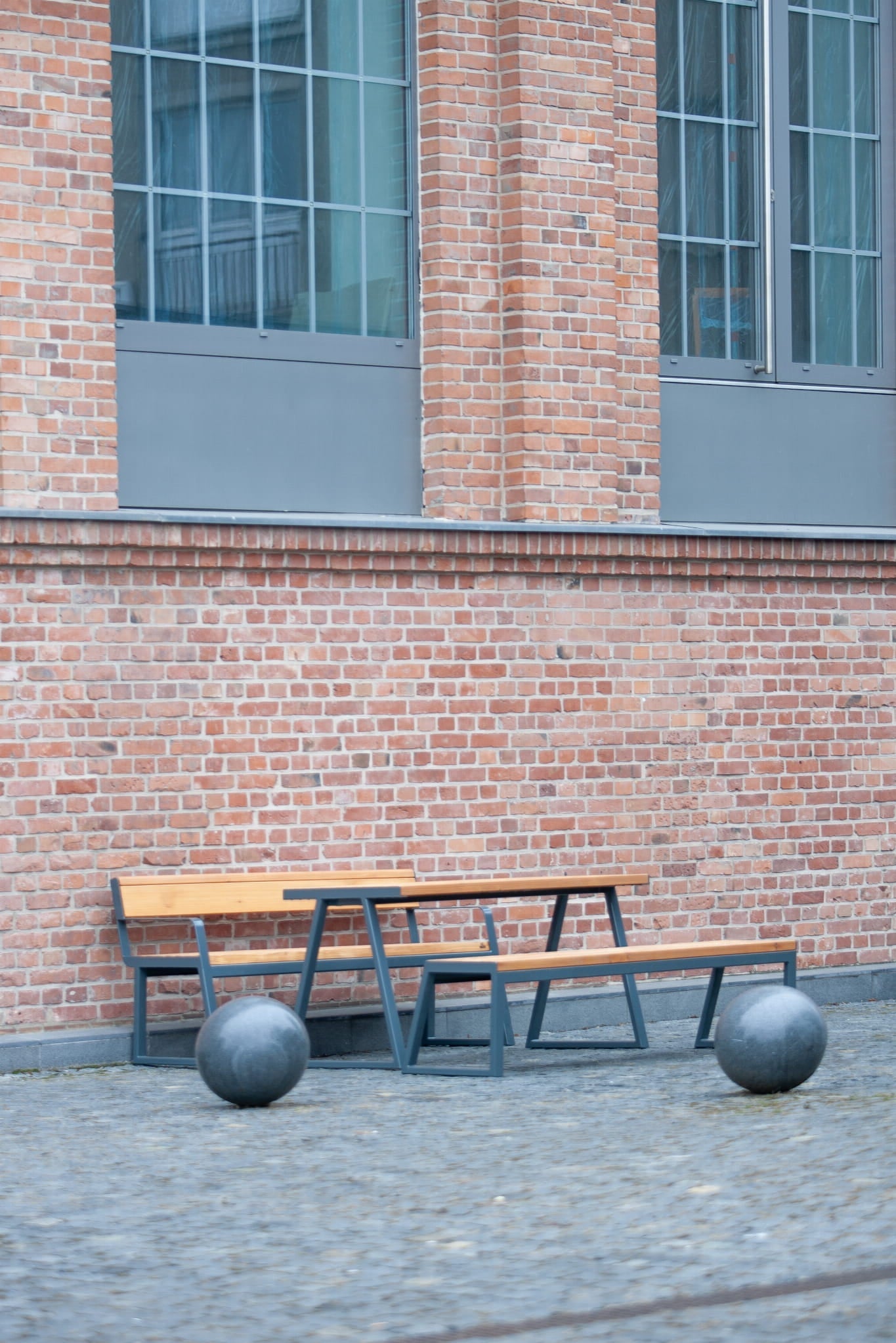 Outdoor wooden table set with metal frame and benches, in front of brick building