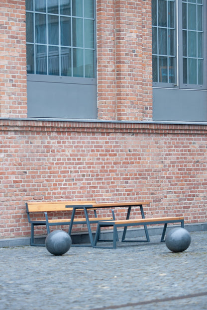 Outdoor wooden table set with metal frame and benches, in front of brick building