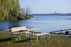 Modern outdoor wooden table with matching benches by a lake on a grassy area