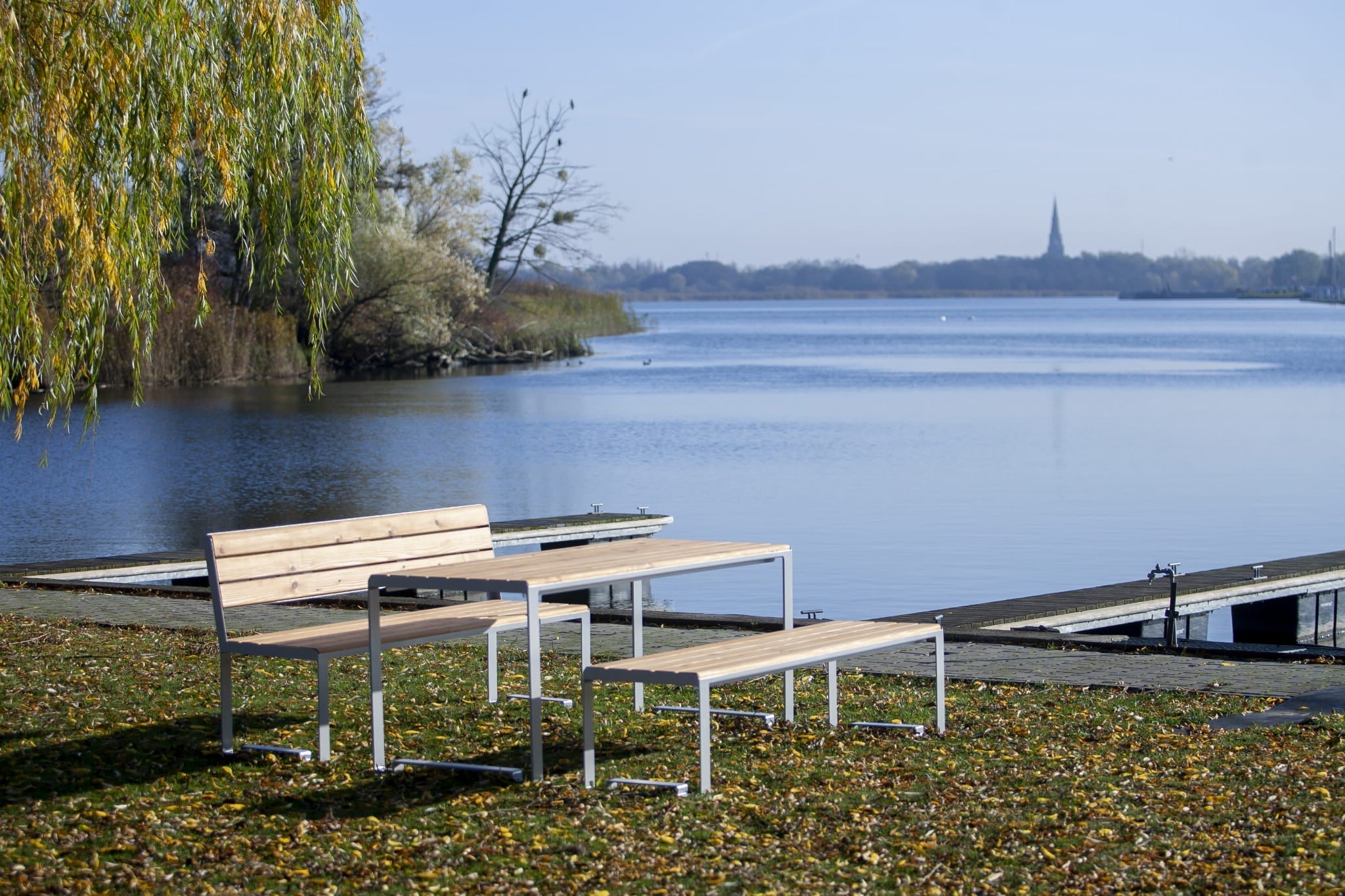Modern outdoor wooden table with matching benches by a lake on a grassy area