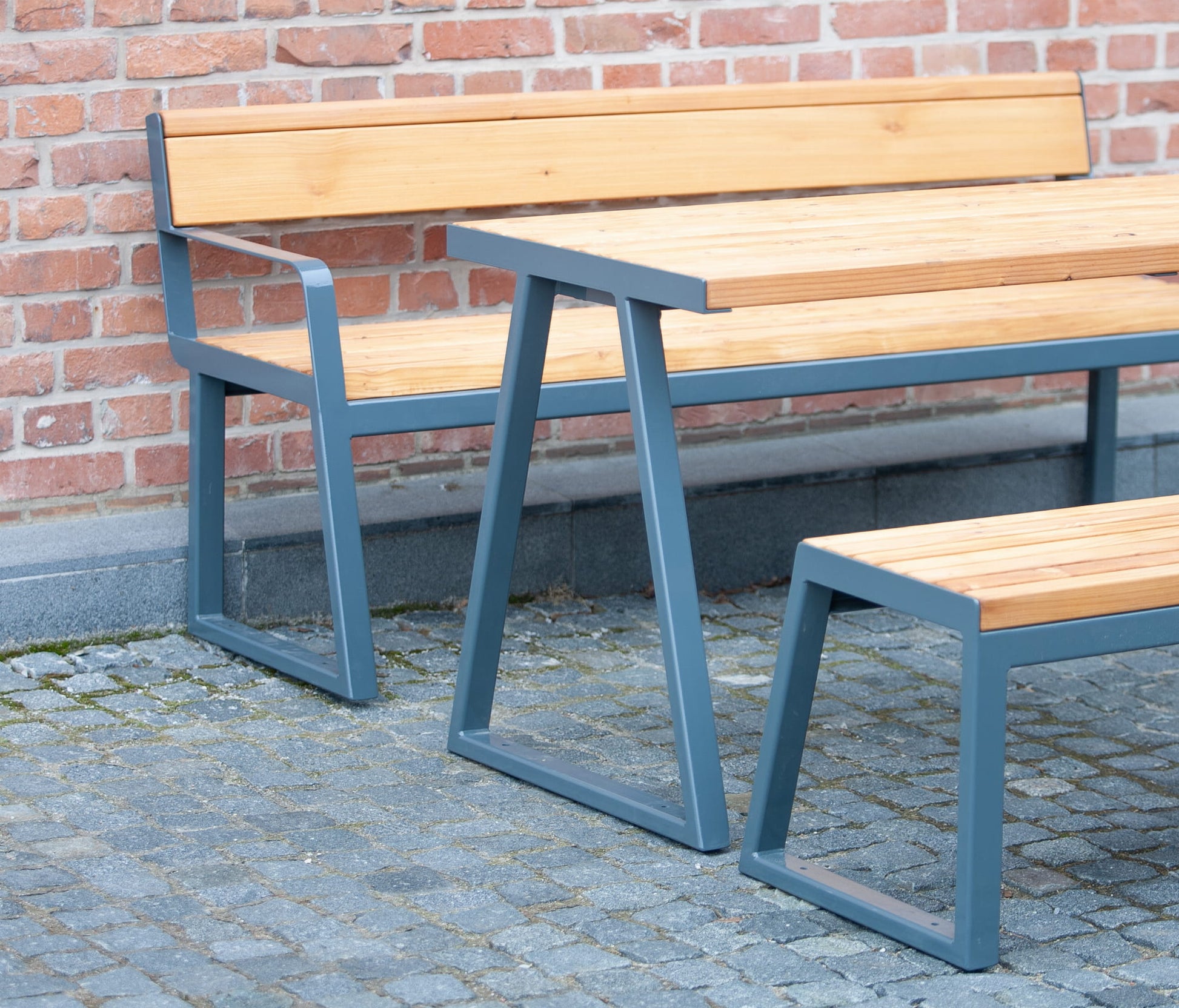 Outdoor wooden table with metal frame, matching bench and seat, set against brick wall