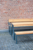 Outdoor wooden and metal table with matching benches on stone patio near brick wall