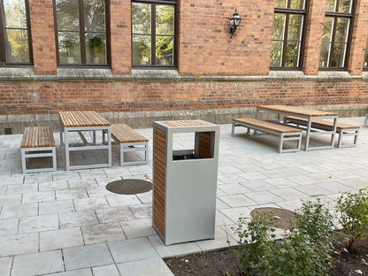 Modern outdoor wastebasket with metal frame and wood panels, surrounded by matching benches and tables on a paved patio.