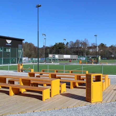 Yellow outdoor wastebasket with matching benches on wooden platform by sports field
