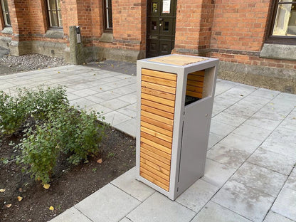 Modern outdoor wastebasket with wood panel design on a paved area near brick building