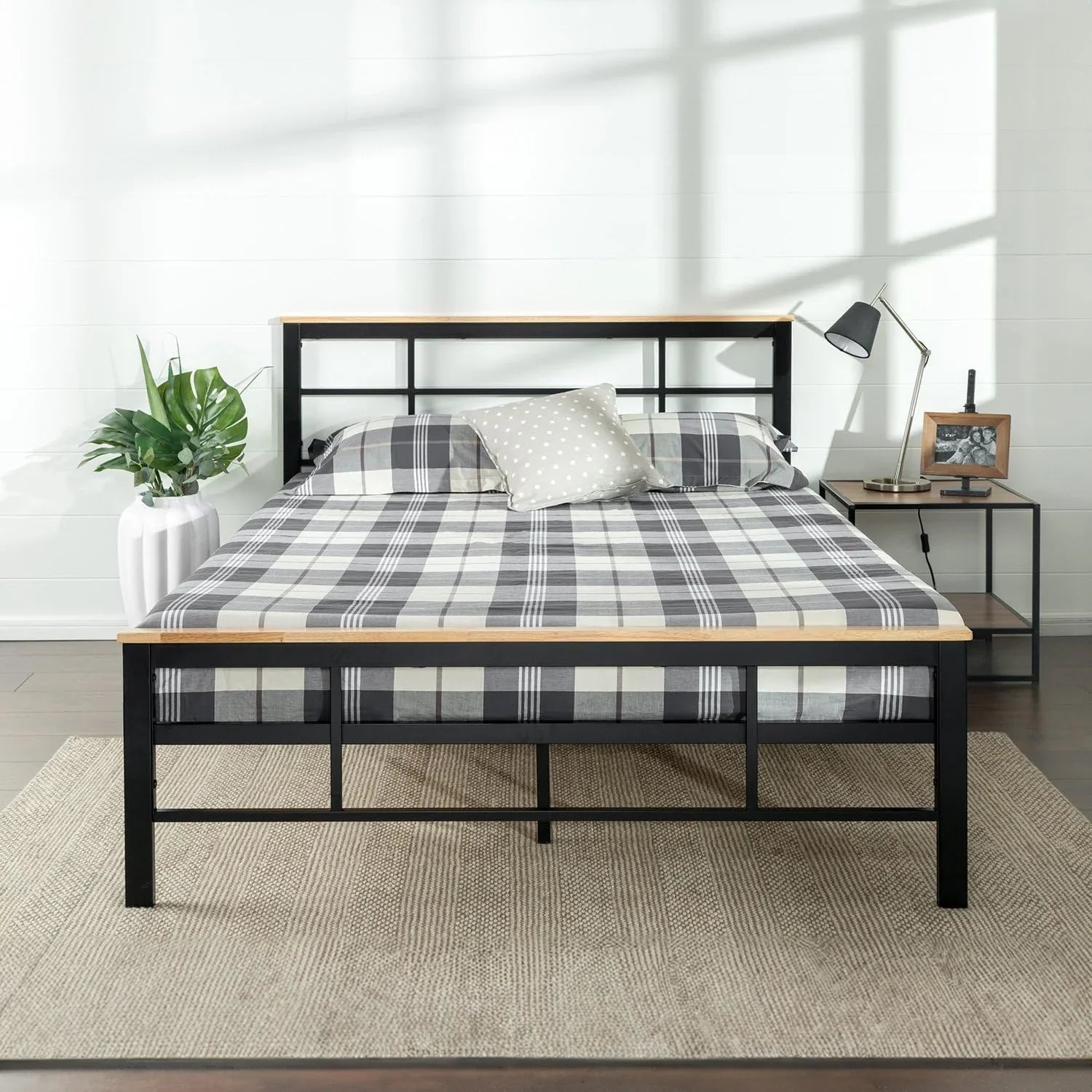Modern steel bed frame with plaid bedding in a bright bedroom, next to a nightstand and plant.